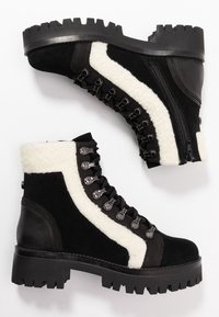 Botas negras con parte superior de ante, forro de espuma blanca, ojales de metal y una suela gruesa de goma negra que presenta un patrón de tracción robusto.