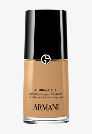 Flaske med Armani Luminous Silk foundation for naturlig glød, med svart lokk og logo på beige bakgrunn.