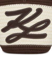 Kudottu olkilaukku, joka sisältää vaalean kermanvärisen pohjan, ruskean nahkakuvion, erottuvan ompelun ja ruskean alaosan.