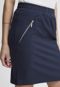 Fustă din material elastic de culoare bleumarin, cu talie elastică și un buzunar cu fermoar pe lateral. Textura netedă și designul adaptat oferă confort și stil.