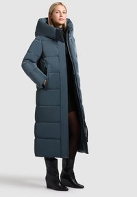 Pikk, pehme ja soe jope tumeteal värviga, millel on kõrge krae, küljetaskud ja luku sulgemine. Kantud musta kleidi peale ja kombineeritud mustade pahklutenäidistega.