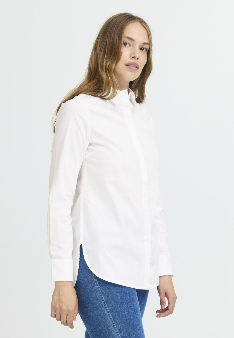 Vit långärmad skjorta med knappar och krage, rak passform, sidofickor och en mjuk textur, tillsammans med blå denimjeans.