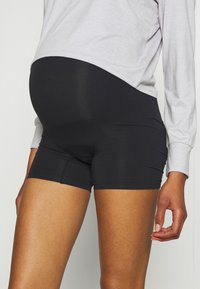 Shorts noirs extensibles conçus pour la maternité, avec une texture lisse et une coupe ajustée, associés à un haut à manches longues gris clair.