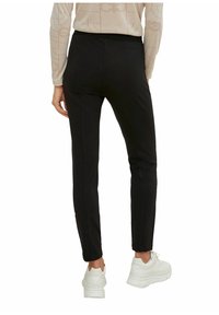 Svarta figurvänliga byxor med en slät yta, som har en elastisk midja och en smal siluett, kombinerade med vita klumpiga sneakers.