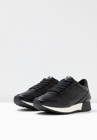 Black athletic shoes featuring a combination of smooth and textured materials, lace-up front, rounded toe, and a chunky white and black sole.