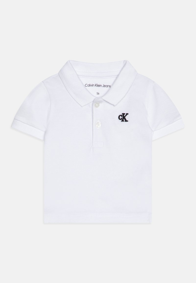 Vit bomullspolo med krage, korta ärmar och en svart broderad "cK"-logotyp på bröstet. Enfärgad tyg, klassisk design.