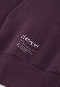 Felpa viola con polsini e orlo a costine. Presenta una scritta bianca con la definizione di "ballerino" stampata sulla parte anteriore in un carattere moderno.