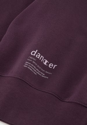 Felpa viola con polsini e orlo a costine. Presenta una scritta bianca con la definizione di "ballerino" stampata sulla parte anteriore in un carattere moderno.