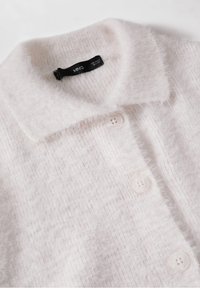 Cardigan en maille douce blanche avec col et trois boutons visibles sur l'ouverture avant.
