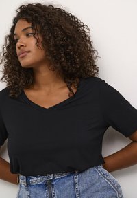 Black V-neck t-shirt with short sleeves, made of smooth material, paired with high-waisted denim shorts featuring a zipper front.