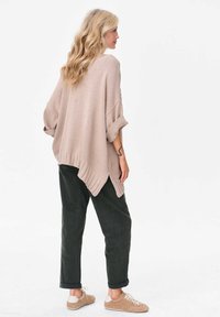 Jasno beżowy, oversize'owy sweter dzianinowy o prążkowanej teksturze i podwiniętych rękawach, w komplecie z ciemnozielonymi spodniami i beżowymi sneakerami.