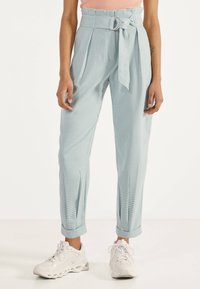 Světle modré kostkované kalhoty se širokými nohavicemi, vysokým pasem a páskem se stříbrnou sponou; doplněné bílými teniskami.