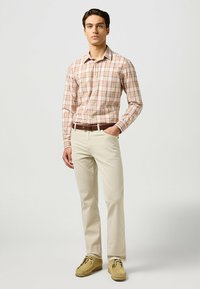Camisa de botón con un patrón de cuadros rojo y beige, combinada con pantalones color crema y calzado marrón claro. Diseño clásico con un corte ajustado.