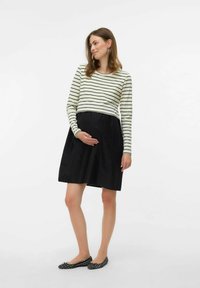 Melnā grūtniecības kleita ar izplestu svārku un gaiši krēma svītrainu garo piedurkņu topu. Tam ir pieguļošs augšdaļa un brīvi kritusi pie jostas.