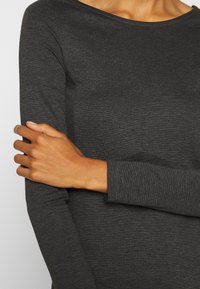 Långärmad topp i mörkgrå ribbad tyg, med rund halsringning och åtsittande ärmar med en mjuk textur. Inga synliga logotyper eller mönster.