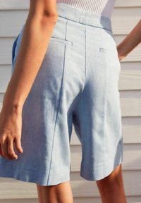 Shorts en lin bleu clair avec une coupe décontractée, poches latérales, et une taille ajustée, présentant une texture subtile et des coutures nettes.