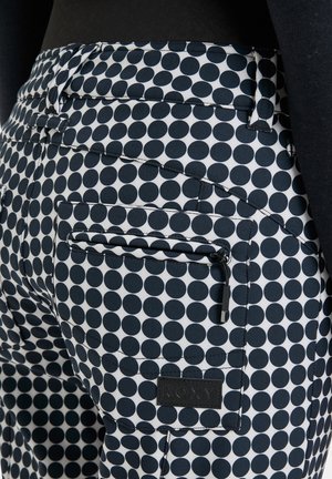 Navy and white polka dot pants with a fitted design, featuring back pockets and a small zipper detail. Material appears smooth and durable.