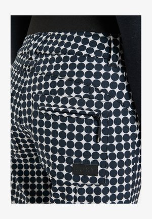 Granatowe spodnie w białe kropki o dopasowanym kroju, z tylnymi kieszeniami i niewielkim detalem w postaci zamka. Materiał wydaje się gładki i trwały.