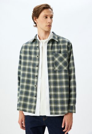 Flannel skjorte i grøn og marineblå tern med knaplukning foran, krave og en lomme på venstre side. Lange ærmer med manchetter.