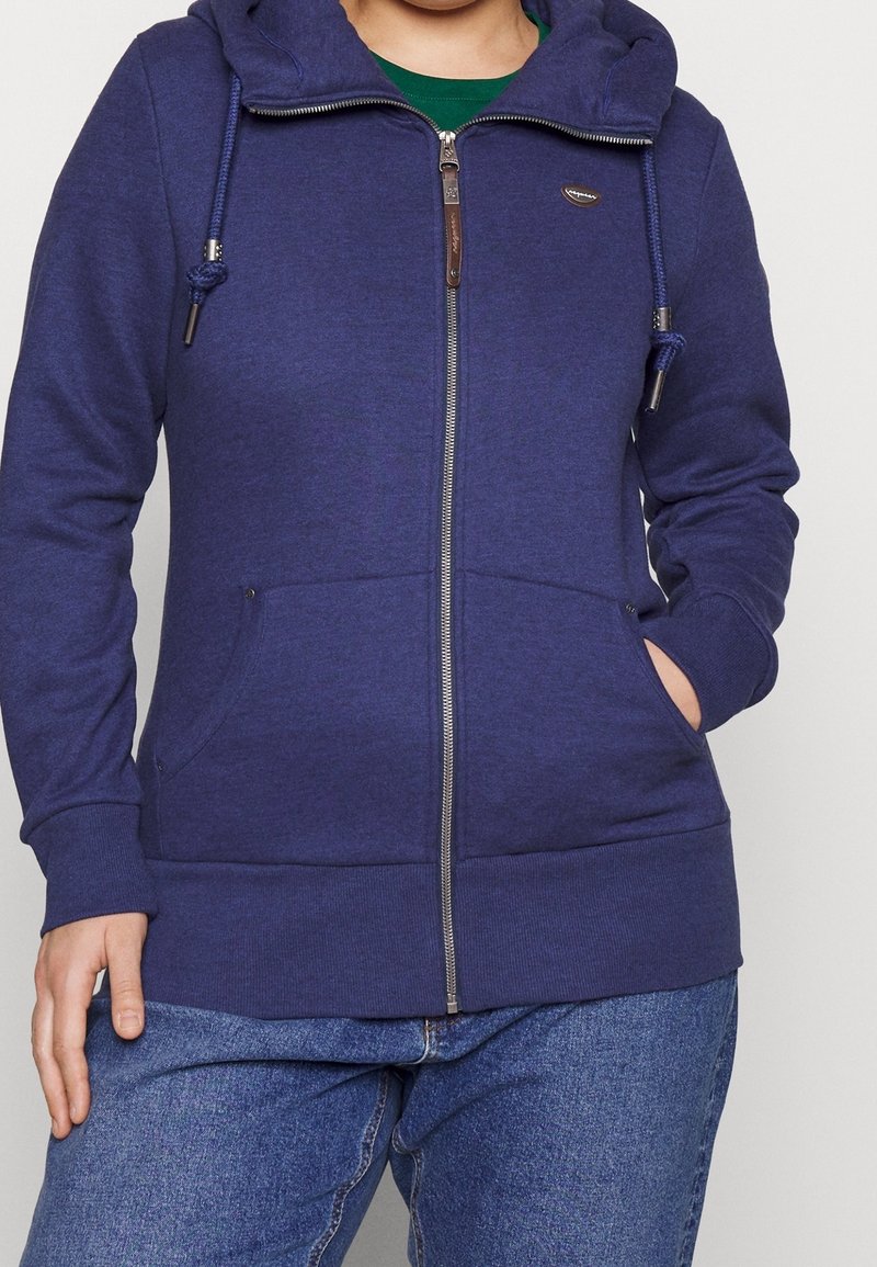 Felpa con zip blu navy in tessuto morbido, dotata di cappuccio regolabile con coulisse, tasche frontali e polsini a costine con dettagli in pelle sulla zip.