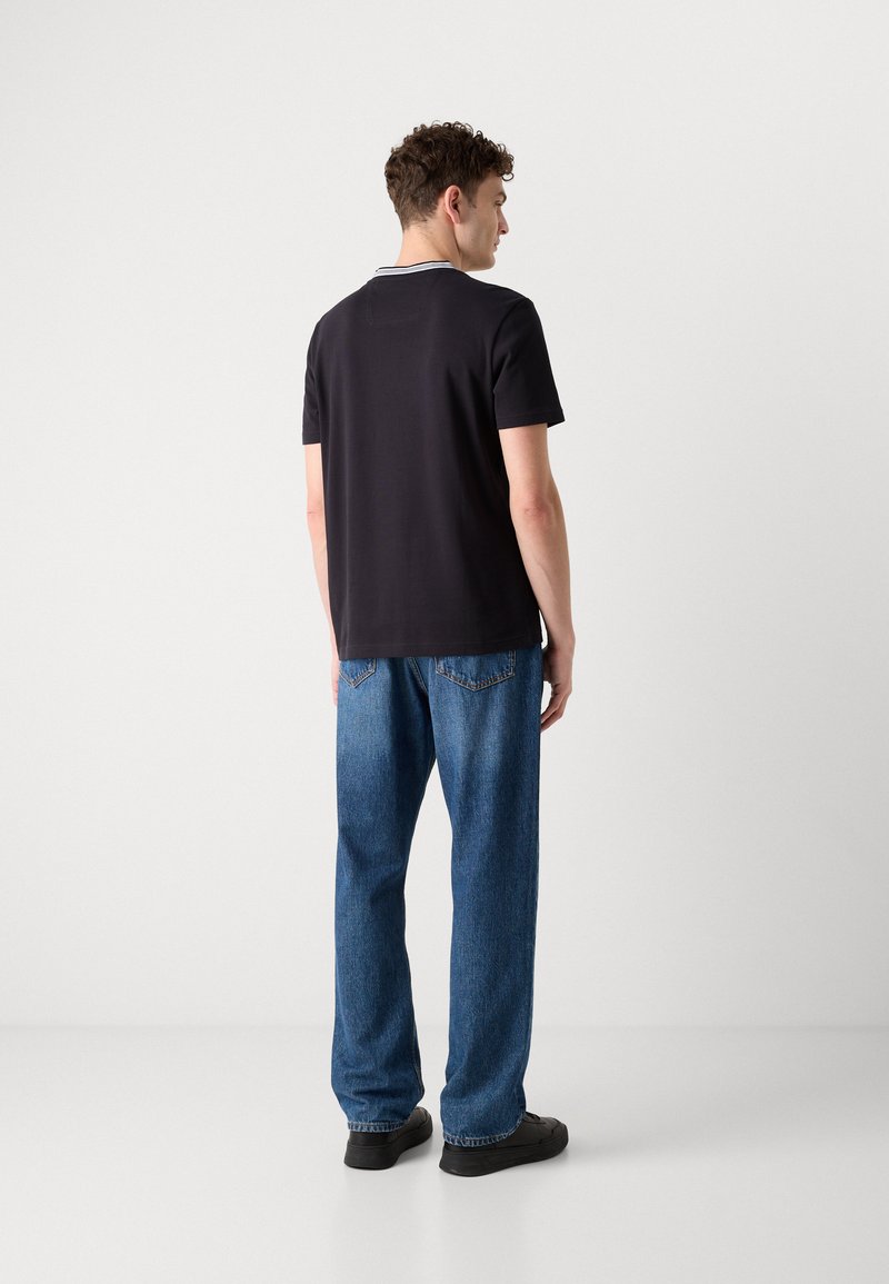 T-shirt noire à manches courtes avec un col contrastant, associée à un jean bleu clair ample et des chaussures noires, vue de dos.