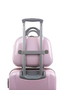 Maleta rígida en rosa claro brillante con un mango gris retráctil y un mango adicional en la parte superior, asegurada con una correa gris.
