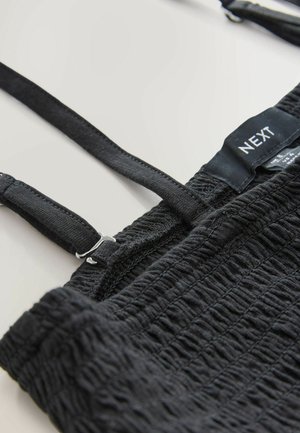 Black smocked top with adjustable straps and silver hardware. Features textured surface with gathered stitching and a brand label.