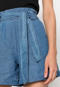 Denim shorts with a light blue hue, featuring a wide waistband with belt loops and a matching tie belt. The material is smooth and textured.