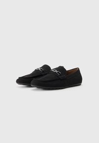 Mocasines de ante negros con un diseño de costura elevada y herrajes decorativos de plata. Suela de goma plana para un uso cómodo.