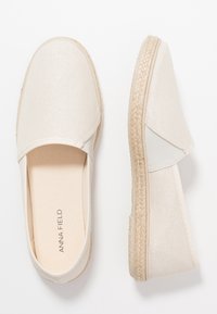 Beige kangastus liugjalatsid tekstuuriga pinnaga, jute tald ja elastsed paneelid lihtsaks jalga panemiseks. Minimalistlik disain ilma kaunistusteta.