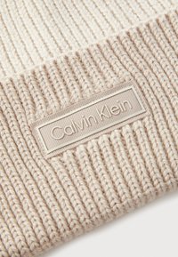 Beige Strickmütze mit geripptem Struktur und aufgenähtem Calvin Klein Logo-Patch, ausgestattet mit einer weichen Garnzusammensetzung und nahtlosem Kantendesign.