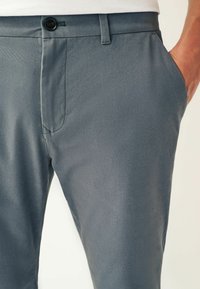 Pantaloni slim fit dintr-un material gri închis, cu închidere buton, buzunare laterale și o textură subtilă, evidențiind linii curate și un design croit.