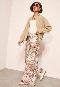Bež oversized jakna, bijeli top bez rukava i lepršave hlače s točkastim uzorkom životinja. Bijele i bež tenisice upotpunjuju outfit.