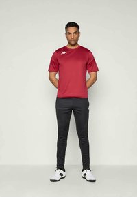 Tricou sportiv roșu cu mâneci scurte, asortat cu pantaloni negri mulați și adidași albi, evidențiind un design minimalist și detalii cu logo.