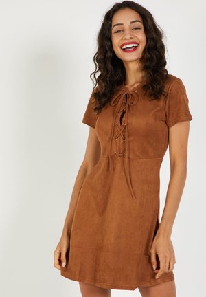 Vestido de ante marrón con mangas cortas, cierre con cordones en la parte delantera y un cuerpo ajustado que lleva a una falda acampanada. Textura suave y un diseño minimalista.