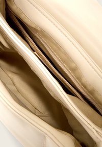 Interno di una borsa a tracolla in pelle beige con due scomparti con zip. Texture liscia con dettagli cuciti e fodera in tessuto morbido.