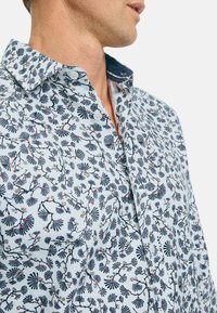 Hellblaues Hemd mit floralen Mustern in Dunkelblau, Rot und Gold, ausgestattet mit einem Button-Down-Kragen und strukturiertem Stoff.