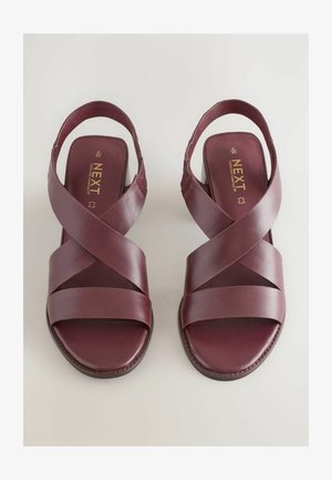 Tamsiai raudoni odiniai šlepetės su kryžminiu dirželiu, atvira nugarine dalimi ir plokščiu padu. Tekstūruota apdaila su matomais siuvinėjimo detalėmis.