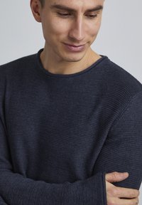Navyblaues, strukturiertes Strickpullover mit rundem Halsausschnitt und langen Ärmeln, ausgestattet mit verlängerten Bündchen und einem feinen Rippenmuster.