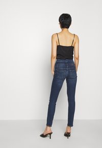 Svart spaghetti strap-topp med låg rygg, kombinerad med högmidjade mörkblå skinny jeans och svarta öppna skor.