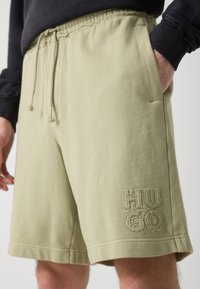 Oliwkowe szorty dresowe z miękkiego materiału, z bocznymi kieszeniami i haftowanym logo "HUGO" na lewym udzie. Elastyczny pasek w talii z sznurkiem.
