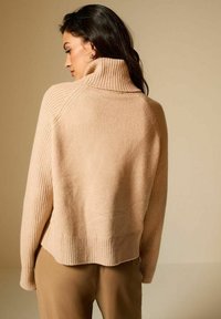 Maglione beige a maglia con colletto alto a coste e orlo a coste, caratterizzato da una texture morbida e una vestibilità rilassata con spalle scese.