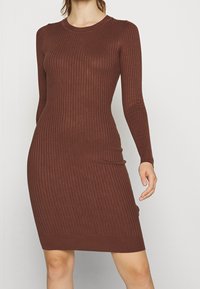 Brun ribbad stickad klänning med långa ärmar, rund halsringning och en kroppsnära silhuett som slutar ovanför knäna med en slät textur.