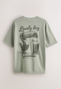 Olivno zelena majica kratkih rokavov z črnim motivom tukana in kozarca piva ter napisom "Lep dan za Guinnessa."