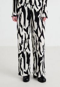 Pantalons plissés à motif noir et blanc, avec une coupe ample, présentant une texture lisse et des ourlets bien finis, associés à des chaussures noires brillantes.