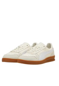 Sneakers bianchi in pelle con profilo basso, superficie testurizzata, perforazioni e suola in gomma marrone. Presentano un logo a striscia bianca sui lati.