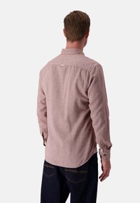 Camicia da uomo a maniche lunghe, tessuto rosa con un motivo strutturato, polsini con bottone, orlo curvo e dettaglio anello sul retro. Indossata con jeans scuri.