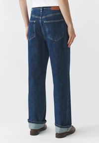 Jeans de mezclilla azul con un corte relajado, dobladillos enrollados y una etiqueta de cuero marrón en la parte posterior de la cintura. Cuenta con dos bolsillos traseros.