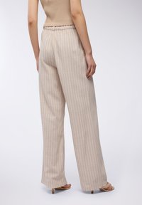 Pantaloni a gamba larga beige a righe con finitura texturizzata e vita elasticizzata, abbinati a tacchi a strappo di colore chiaro.