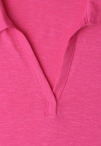 Gros plan d'une chemise rose vif à col avec une ouverture en V et un tissu tricoté texturé.